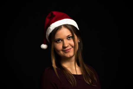 Pretty young woman, smiling, wearing red hut, purple dress, on black background, low-keyの写真素材