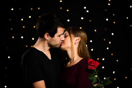 young couple, man and woman, on black background, holding red rose and kissingの写真素材