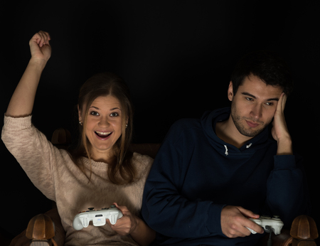 Young couple, man and woman play computer games sitting in dark room in front of tv or monitor, holding game controllers in their handsの写真素材