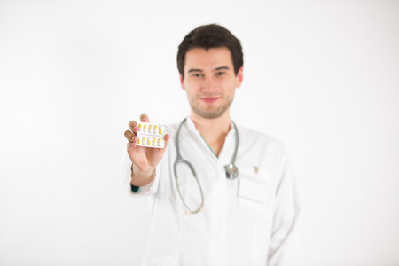 young male doctor, on white background, wearing white coat, holds colorful tabletsの写真素材