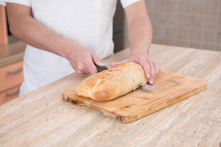 young male cook cuts ciabatta bread