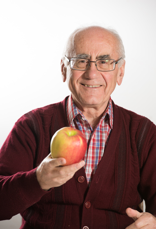 old seniour man holding fresh apple and smiling, wearing eyeglasses wearing red sweaterの写真素材