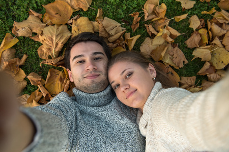 young couple in the park, in love, making selfie, lying on the green grass and yellow leavesの写真素材