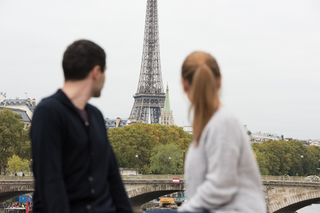 young couple man and woman sitting on the bridge on river Seine, Paris, France, in front of Eiffel Towerの写真素材