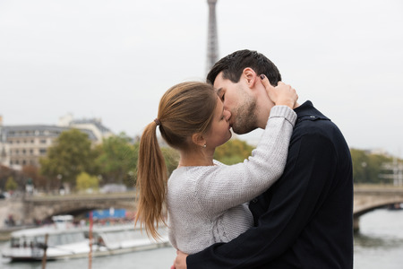 young couple man and woman sitting on the bridge on river Seine, Paris, France, in front of Eiffel Tower, kissingの写真素材