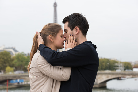 young couple man and woman sitting on the bridge on river Seine, Paris, France, in front of Eiffel Tower, kissingの写真素材