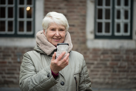 Elderly woman wearing winter clothes uses smartphone makes selfiesの写真素材