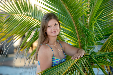 pretty young woman wearing bikini standing under the palm tree on the beach in Florida, USAの写真素材