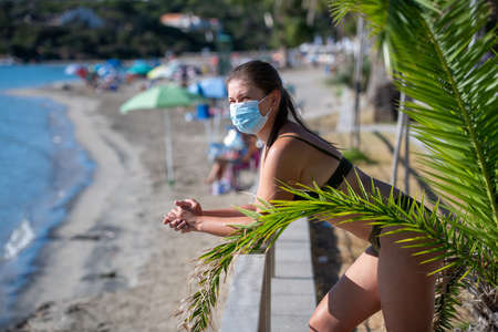 Young woman relaxing at the beach with a face mask protection and practicing social distancingの写真素材