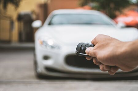 The man opens the car with a keychain, in the background is a white car