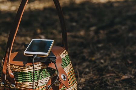 Mock up of a smartphone with charging Power Bank on a basket in the forest. Concept on the theme of outdoor recreationの写真素材