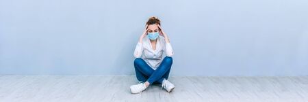 Banner Girl with a medical mask sitting on the floor against the background of a gray wall. The concept on the theme of coronavirus COVID-19の写真素材