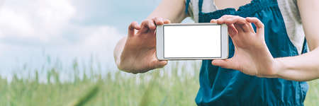 Banner, Mock up of a smartphone in the hands of a girl farmer, against the background of a green...