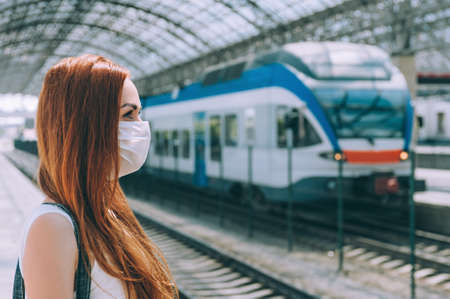 Girl, in a medical mask, at the station. Against the background of a modern train.