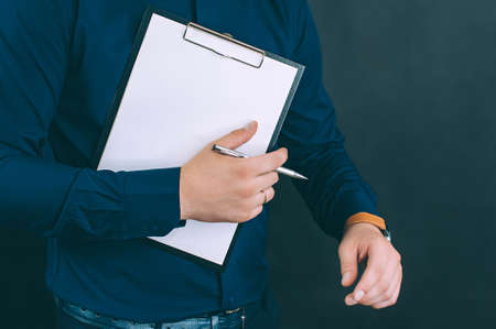 Businessman with a folder for documents and a watch in his hands, on a black backgroundの写真素材