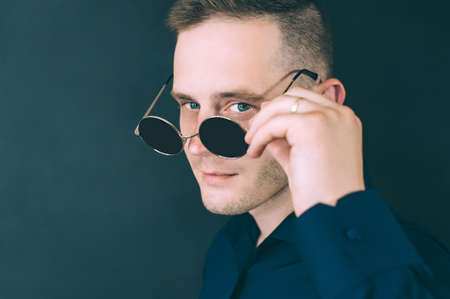 husband flirts, looks through glasses. against a dark backgroundの写真素材