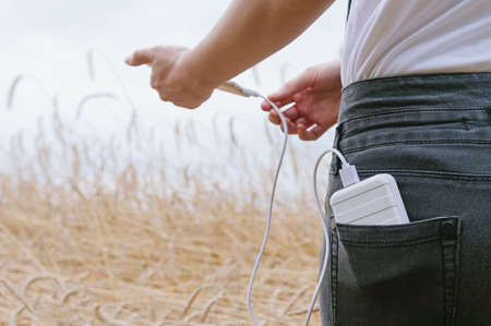 The girl in the yellow field, charges the phone from power bank.