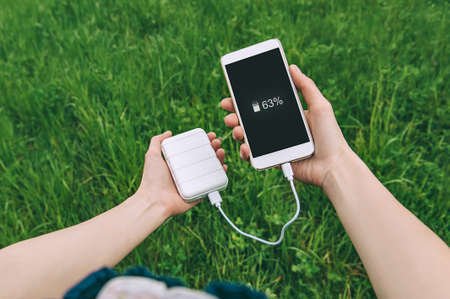 close-up of charging the phone from the power bank in the hands of the girl. against the backdrop of natureの写真素材