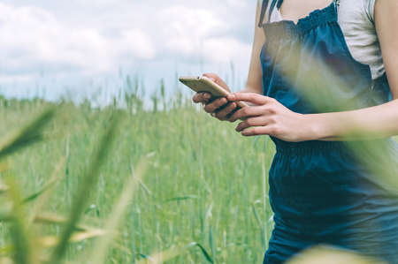 Mock up of a smartphone in the hands of a girl farmer, against the background of a green field.の写真素材