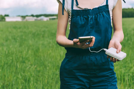 close-up of charging the phone from the pover bank in the hands of a farmer girl. against the background of agricultureの写真素材