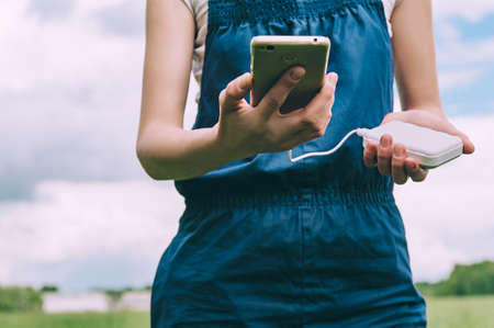close-up of charging the phone from the pover bank in the hands of a farmer girl. against the...