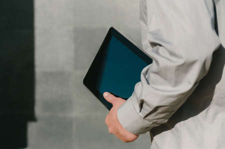 Tablet in the hands of a walking man, Close-up. against the background of a concrete wall with a shadowの写真素材