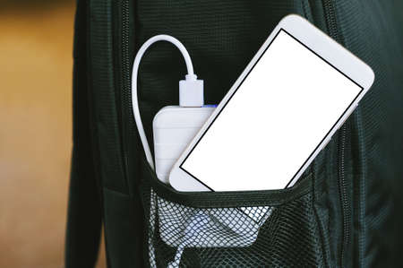 A power bank charges a smartphone in a pocket of a black backpack. on a light yellow backgroundの写真素材
