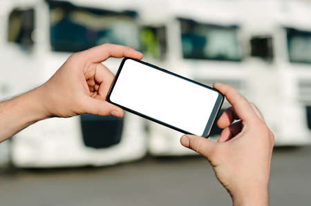 Mock up of a smartphone in the hands of a man. Against the backdrop of trucks. Logistics conceptの写真素材