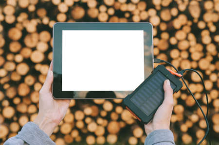 Mockup of a tablet in the hands of a girl with a charger from a power bank. Against the background of a round forestの写真素材