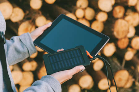 Power Bank with solar glass in the girl's hand, on the background of the tablet and timber harvestingの写真素材