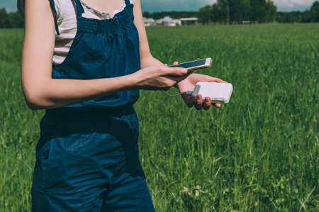 Power Bank in the hands of a girl charges a smartphone. against the background of the green field of...