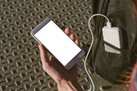 Mock up of a smartphone in a man's hand. Charging from a power bank in a backpack pocketの写真素材
