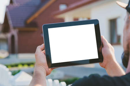 Close-up of a tablet in the hands of a man, on the background of the house
