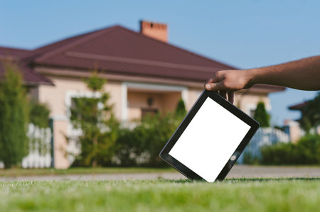 Tablet in hand, on the lawn against the backdrop of the houseの写真素材