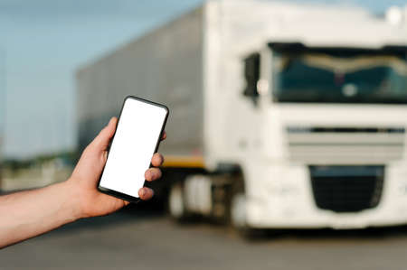 Mock up of a smartphone in a man's hand. Against the backdrop of trucks. Logistics conceptの写真素材