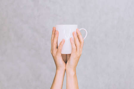 White mug for coffee, tea in the hands of a girl. On a white backgroundの写真素材
