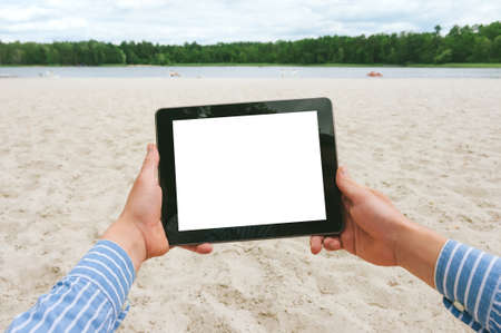 Mock up tablet in the hands of a man. Against the backdrop of the beach and forest riverの写真素材