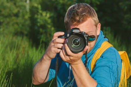 Close-up, the photographer holds a professional photo-video camera in his hands. Against the background of green beautiful natureの写真素材
