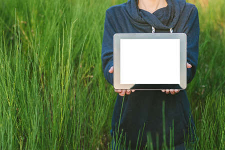 A girl in a gray sweater holds a tablet mockup in her hands. against the backdrop of beautiful natureの写真素材