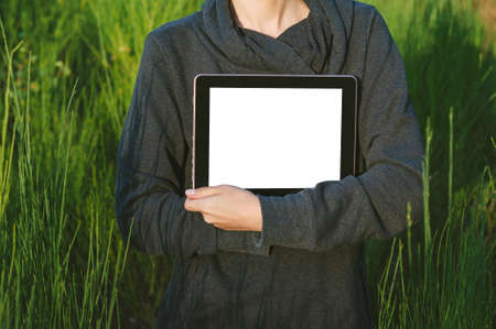 A girl in a gray sweater holds a tablet mockup in her hands. against the backdrop of beautiful natureの写真素材
