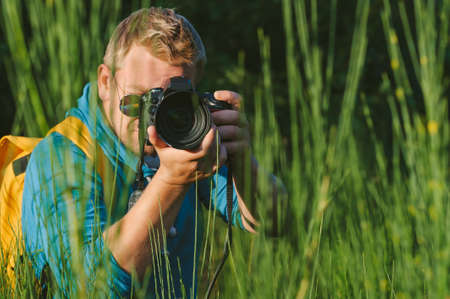 Close-up, the photographer holds a professional photo-video camera in his hands. Against the background of green beautiful natureの写真素材