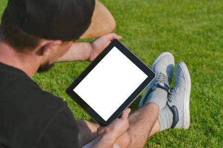 Mockup tablet in the hands of the guy. Against the backdrop of a green lawnの写真素材