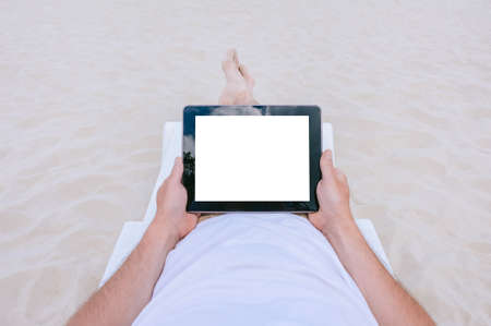 Mock up tablet in the hands of a man lying on a sun lounger on the beach. Against the background of sandの写真素材