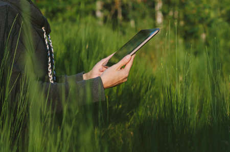 A tablet in the hands of a girl close-up. against the background of green natureの写真素材