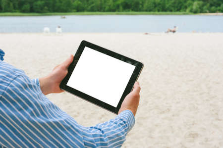 Mock up tablet in the hands of a man. Against the backdrop of the beach and the riverの写真素材