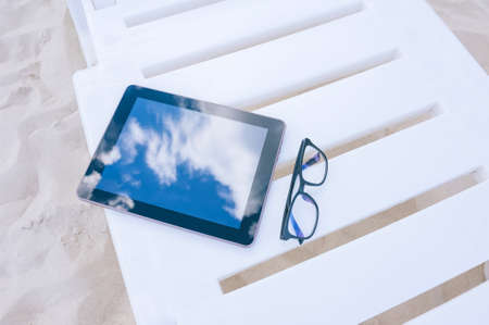 The mock-up of the tablet lies on a sun lounger with glasses. Against the backdrop of beach sand. Travel conceptの写真素材
