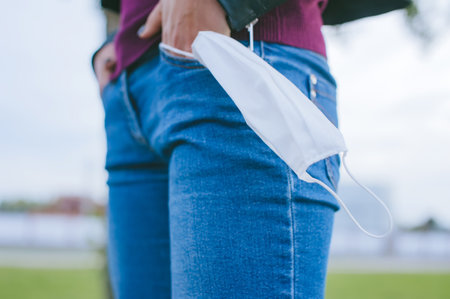 Hand with a mask in the pocket of a girl's jeans. against the background of the city lawn. Stop virus conceptの写真素材