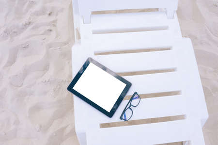 The mock-up of the tablet lies on a sun lounger with glasses. Against the backdrop of beach sand. Travel conceptの写真素材