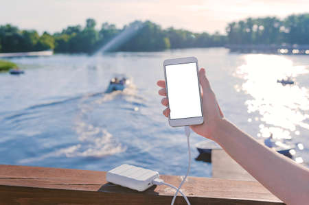 Mock up of a smartphone in the hand of a girl on the pier. Charge your phone with Power Bank....