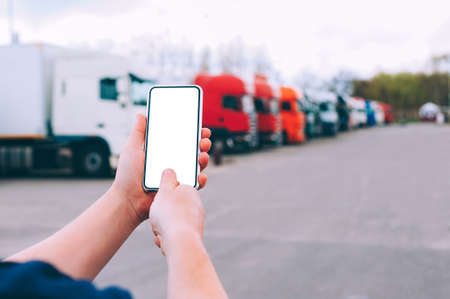 Mock up a smartphone in the hands of a man. Against the background of red trucks. Logistics conceptの写真素材
